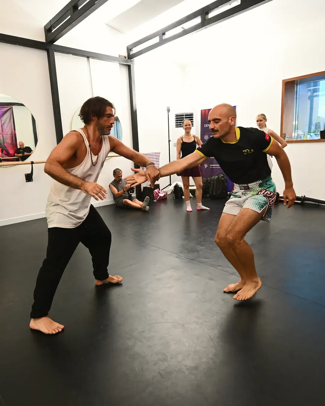 Beyaz duvar önünde eşli refleks çalışması yapan iki muay thai eğitmeni