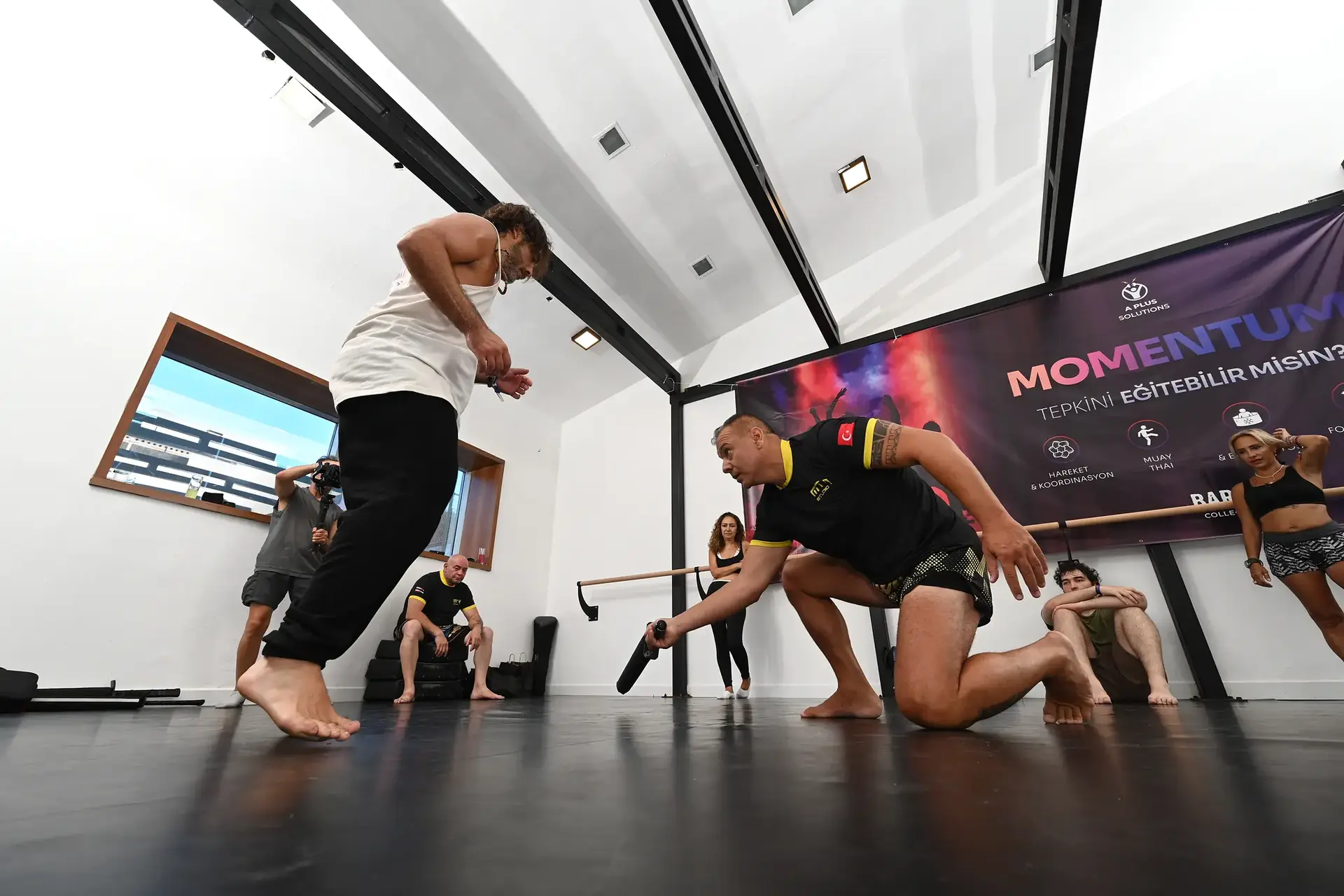 Çömelip sopayla refleks çalıştıran muay thai koçu